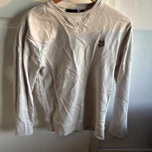 Beige tröja från Lyle & Scott - Säljer en stilren beige tröja från Lyle & Scott med deras ikoniska logga på bröstet. Tröjan har långa ärmar och en rund halsringning med ribbade detaljer. Bara använd ett fåtal gånger. Pris kan diskuteras vid snabb affär. 