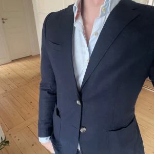Mörkblå kavaj från Strömberg - Snygg mörkblå kavaj från Strömberg med klassisk design. Fläck på ärmen som nog går att tvätta bort, har inte testat ännu. Storlek 46. Passar perfekt på sommaren och mindre formella tillställningar.