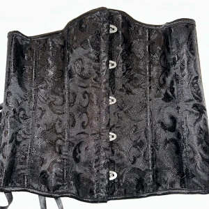 Svart Underbystkorsett - En väldigt fin underbyst korsett som har 14 formstavar i hårdplast, hyskknäppning framtill och dragsko bak. Ger ett bra stöd för ryggen och fin kroppshållning. Supersnygg att ha ovanpå en skjorta, T-shirt eller klänning. Produkten är testad och fotad, men inte använts på ett sätt som påverkar dess skick eller funktion. 