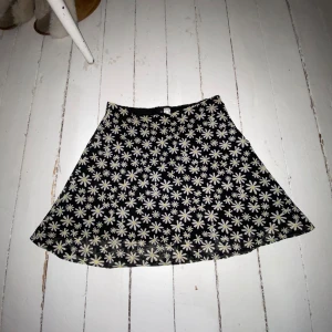 Svart blommig kjol från Divided - Säljer en svart kjol från HM med ett härligt sommrigt blommönster i vitt och gult. Kjolen har en avslappnad passform och är perfekt för en midsommar med släkten, eller bara en vanlig skoldag. Den är tillverkad i ett lätt, luftigt och bekvämt material.