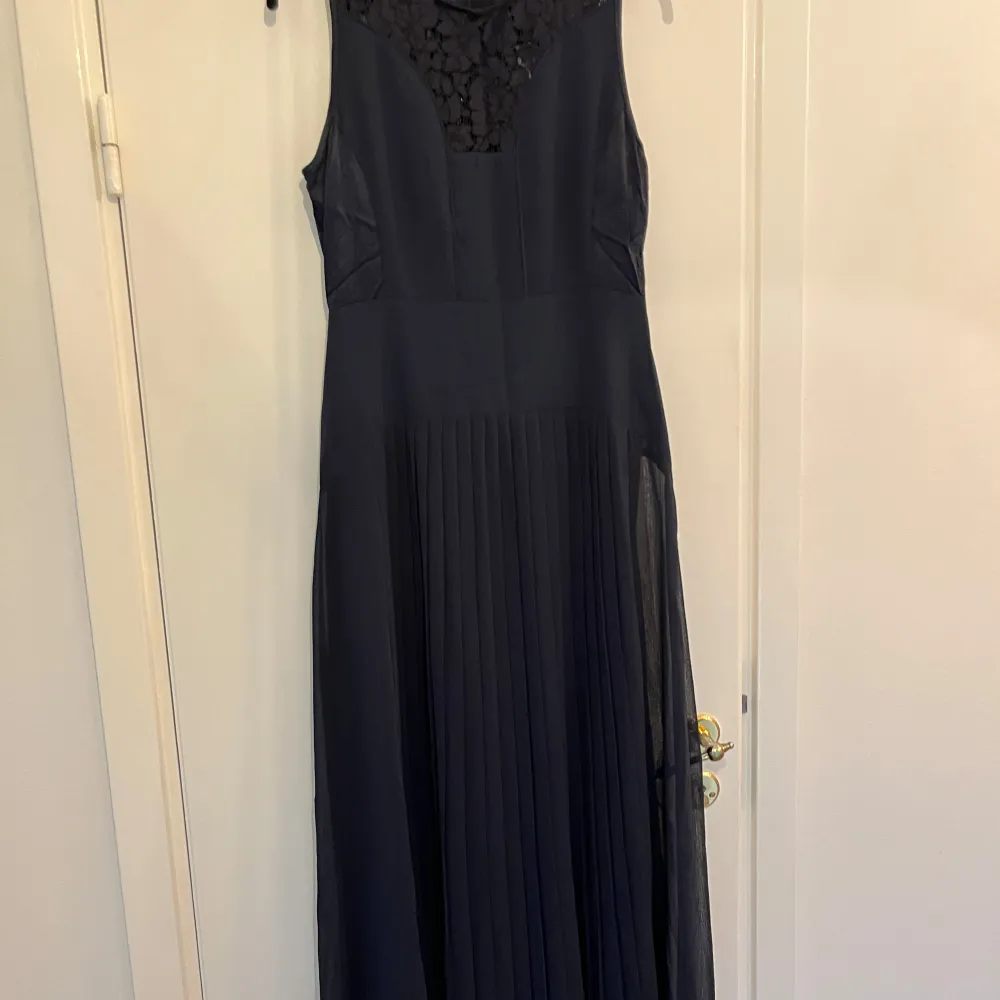Elegant mörkblå långklänning från InWear med vackra spetsdetaljer på överdelen. Klänningen är ärmlös och har en dragkedja i ryggen. Tillverkad i polyester med viskosfoder för en bekväm passform. Perfekt för en stilfull kväll.. Mekot.