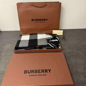 Rutig halsduk från Burberry - Snygg och lyxig halsduk från Burberry i svart och grått rutmönster. Tillverkad i 100% kashmir för en mjuk och varm känsla. Perfekt för att hålla stilen under kyliga dagar. Kommer med originalförpackning och etikett. Rekommenderas starkt här på Skagen_chloting_ressel_Uf👍✅😉