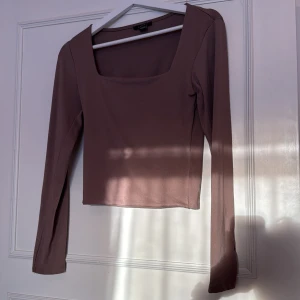 Brun långärmad topp - Säljer en stilren brun topp med långa ärmar och fyrkantig halsringning. Perfekt för en chic och enkel look. Toppen är i ett mjukt och bekvämt material. Dubbelt tyg på framsidan om man inte vill ha bh på sig