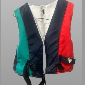 Flerfärgad flytväst - Säljer en flerfärgad flytväst med paneler i rött, grönt och blått. Västen har en dragkedja framtill och justerbara remmar för en säker passform. Perfekt för vattensporter och båtturer.