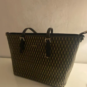 Vabene handväska - Snygg axelväska från Vabene med ett unikt mönster i svart och beige. Väskan har svarta handtag och silverfärgade detaljer. Perfekt för skolan eller jobb.