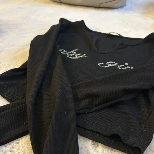 Svart ribbad topp från Shein - Snygg svart ribbad topp från Shein med texten 'baby girl' i glittriga stenar på framsidan. Perfekt för en trendig look.