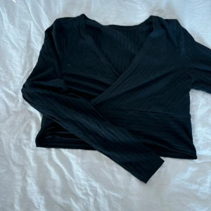 Svart omlottopp - Snygg svart omlottopp med långa ärmar och ribbad struktur. Perfekt för en stilren look.