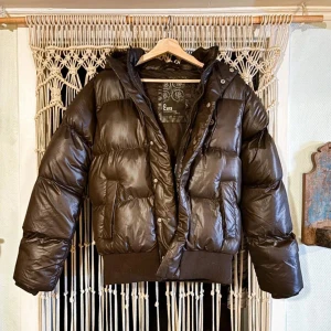 Mörk brun pufferjacka med päls - Pufferjacka med avtagbar päls. Jackan har dragkedja och knappar framtill för extra skydd mot kyla. Storlek S 