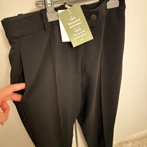 Svarta kostymbyxor från H&M - Snygga svarta kostymbyxor från H&M i återvunnen polyester. Byxorna har en klassisk design med hög midja och knappstängning. Perfekta för en stilren look.