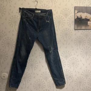 Blå jeans med slitningar - Snygga blå jeans med slitningar för en trendig look. De har en klassisk femficksdesign och är perfekta för en avslappnad stil. Passformen är smal och de är tillverkade i ett bekvämt denimtyg.