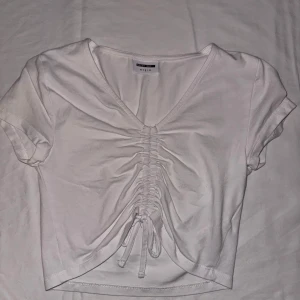 Vit kortärmad topp från Bershka - Säljer en vit kortärmad topp från Bershka med v-ringning och snygg snörning framtill. Perfekt för en stilren och trendig look. Passar bra till både jeans och kjol.