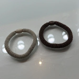 Två tofsar/armband i beige och brun - Säljer två tofsar/armband, ett i beige och ett i brun färg. De är enkla och stilrena, perfekta för vardagsbruk. Dom är mjuka och är bekväma att bära. Använda få antal gånger. Köpt dom för 20 kr för en. Så dom kostade 40 kr båda två. 