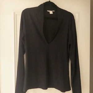 Svart långärmad tröja från H&M  - Säljer en stilren svart långärmad tröja med v-ringning. Perfekt för en minimalistisk look och passar bra till både jeans och kjol. Ett mångsidigt plagg för garderoben.