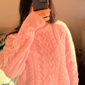 Rosa stickad tröja - Mysig rosa stickad tröja med kabelstickat mönster. Perfekt för kyliga dagar med sin varma och bekväma design. Tröjan har långa ärmar och en hög krage som ger extra värme.