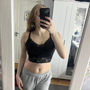 Svart spetslinne - Snyggt svart spetslinne med smala axelband och en croppad passform. Perfekt för en trendig look.