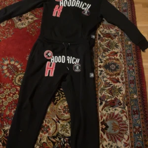 Svarta mjukisbyxor från Hoodrich - Snygga svarta mjukisbyxor från Hoodrich med vita och röda detaljer. Byxorna har snörning i midjan och en dragkedjeficka. Perfekta för en avslappnad stil.