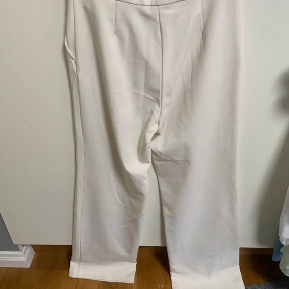 Snygga vita kostymbyxor med hög midja och rak passform. Perfekta för en stilren look. Byxorna har en klassisk design med veck framtill och uppvikta benslut.. Farkut & Housut.