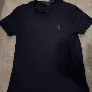 Mörkblå t-shirt från Polo Ralph Lauren - Tja, säljer nu en Snygg mörkblå t-shirt från Polo Ralph Lauren. Tröjan har inga defekter eller likande och är jättebra skick! Hör av er vid eventuella frågor eller funderingar.