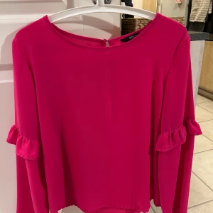 Rosa blus från ONLY - Säljer en snygg rosa blus från ONLY med långa ärmar och volangdetaljer vid ärmsluten. Perfekt för att liva upp garderoben med en färgklick!