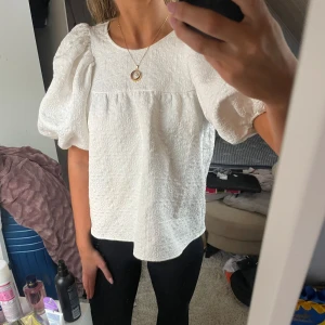 Vit blus från & Other Stories - Säljer en elegant vit blus från & Other Stories med puffiga kortärmar och en texturerad yta. Perfekt för en stilren look. Blusen har en rund halsringning och en diskret dragkedja i ryggen.