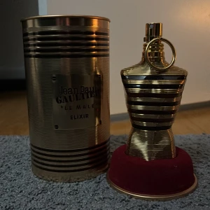 Jean Paul Gaultier Le Male Elixir - Säljer en elegant parfymflaska från Jean Paul Gaultier, Le Male Elixir. Flaskan har en unik design i form av en manlig torso med guld- och svartfärgade ränder. Den kommer i en stilren metallburk med märkets logotyp. Perfekt för den som vill ha en distinkt och lyxig doft. Parfymen är 75ml med ca 85% kvar.