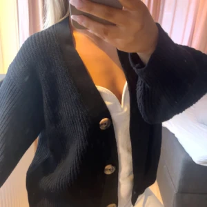 Svart kofta med knappar - Säljer en stilren svart kofta med stora knappar framtill. Perfekt för lager-på-lager och passar till många olika outfits. Koftan har en klassisk design med långa ärmar.