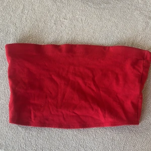 Röd tubtopp - Säljer en enkel och stilren röd tubtopp. Perfekt för sommardagar eller som ett basplagg i garderoben. Tillverkad i ett mjukt och stretchigt material för en bekväm passform.