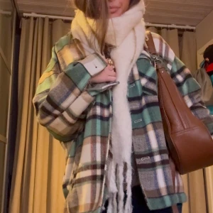 Rutig kappa från Zara - Snygg rutig kappa från Zara i gröna, bruna och beiga toner. Jackan har knappar framtill och två bröstfickor med lock. Perfekt för lager-på-lager-stil under höst och vår.