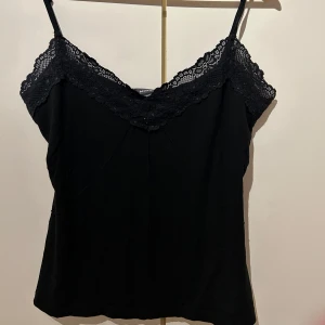 Svart linne - Elegant svart linne med spetsdetaljer längs urringningen och tunna axelband. Finns små svarta diamanter på tröjan. 