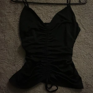 Svart linnetopp från Gina Tricot - Snygg svart linnetopp från Gina Tricot med smala axelband och rynkdetaljer framtill. Perfekt för en stilren look.