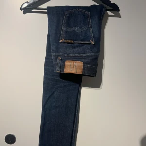 Mörkblå jeans från Nudie  - Snygga mörkblå jeans från nudir med klassisk femficksdesign och en diskret logga på bakfickan. Perfekta för en stilren look. Jeansen har en rak passform och är tillverkade i ett slitstarkt denimtyg.
