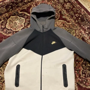 Grå,svart,vit xl  har försökt att få bort smutser men gick inte bort - Säljer en snygg grå och svart hoodie från Nike med dragkedja och huva. Jackan har en klassisk design med Nike-logga på bröstet och praktiska fickor med dragkedjor. Perfekt för en avslappnad stil.