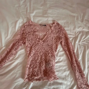 Rosa spetsblus från Gina Tricot - Säljer en söt rosa spetsblus från Gina Tricot. Blusen har en v-ringad design och långa ärmar, perfekt för en romantisk look. Den är tillverkad i ett vackert spetsmaterial som ger en elegant touch.