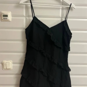 Kort svart volang klänning från Shein storlek:L - Snygg svart klänning från Shein med volangdetaljer och smala axelband. Perfekt för en stilren look. Klänningen har en omlott-design som ger en elegant touch. Aldrig använd och lapp finns kvar på klänningen. Köpte från SHEIN och jag säljer för 145 kronor.✨