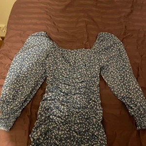 Blommig blå klänning från Shein - Säljer en söt blå klänning från Shein med vita blommor. Klänningen har långa ärmar och en dragkedja på sidan. Perfekt för en somrig look! 🌸