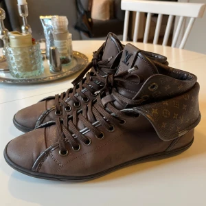 Louis Vuitton Brown Leather Brea High Top Sneakers - Dessa ursnygga high top sneaker från Louis Vuitton kommer med en dubbelvikt hi-top. De är gjorda av brun kalvskinn och accentueras med monogramduk. Dessa snörskor har gummisulor, LV-logotyper och läderfodrade innersulor.💕