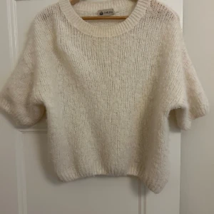 Vit stickad tröja från Chelsea - Mysig vit stickad tröja från Chelsea med korta ärmar.. Tröjan har en rund halsringning och är gjord i ett fluffigt material som ger en skön känsla.