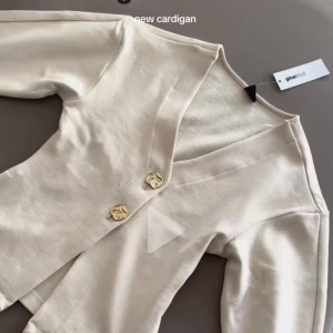 Vit kofta från Ginatricot - Säljer en stilren vit kofta från Ginatricot med dekorativa knappar framtill. Koftan har en v-ringad design och långa ärmar, perfekt för en elegant look.använd en gång för egna bilder kontakta privat säljer pågrund av fel storlek dene helt slutsåld där med priset 