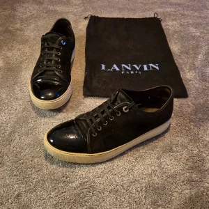 Lanvin skor - Snygga svarta sneakers från Lanvin med glansiga detaljer på tån och snörning. Skorna har en vit sula och kommer med en svart förvaringspåse. Perfekta för en stilren look.