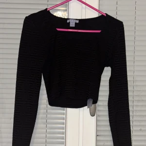 Svart långärmad topp från new yorker  - Snygg svart långärmad topp från new yorker  med ett diskret geometriskt mönster. Toppen är croppad och har en tight passform, perfekt för en stilren look. Passar bra till både jeans och kjol.