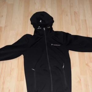 Svart  zip hoodie Peak Performance - Säljer en svart zip hoodie från Peak Performance med dragkedja och huva.  Den har en enkel och stilren design med logotyp på bröstet.