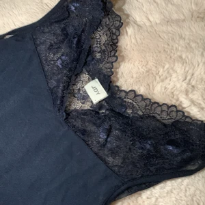 Mörk blå linne från JDY med spetsdetaljer - Snyggt svart linne från Joy med vackra spetsdetaljer vid axlarna och halsringningen. Perfekt för att lägga till en elegant touch till din outfit.