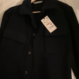 Svart overshirt från Zara - Snygg svart overshirt från Zara med knappar framtill och två stora bröstfickor. Perfekt för lager-på-lager-stil. Enkel och stilren design som passar till många tillfällen.