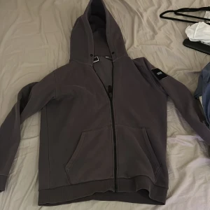 Grå hoodie från Jack & Jones - Säljer en stilren grå hoodie från Jack & Jones. Den har en dragkedja framtill och en praktisk huva. Perfekt för en avslappnad stil.