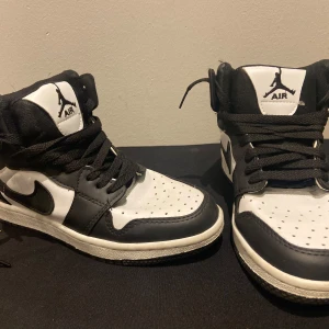Svarta och vita Nike Air Jordans - Säljer ett par klassiska Nike Air Jordans i svart och vitt. Skorna har en hög design med snörning och den ikoniska Air Jordan-loggan på plösen. Perfekta för dig som vill ha en stilren och sportig look.