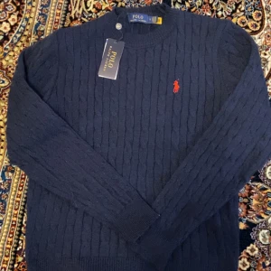 Mörkblå kabelstickad tröja från Ralph Lauren - Säljer en Ralph lauren sweater. Fick den som födelsedagspresent och den har varit för liten. Den är knappt använt och är i helt ny skick. Den är billig och kan meddelas vid snabb affär.