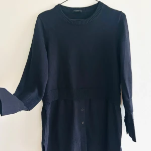 Marinblå långärmad tröja/skjorta från COS - Säljer en stilren marinblå tröja från COS. Finstickad i 100% ull med halvlång ärm och kort liv. Den stickade tröjan övergår i ärmar och nederdel i skjortmaterial 100% bomull med struktur. Ärmarna har skjortknäppning i ärmslut och den knälånga nederdelen har knappar framtill. Rak och lite vidare i modellen. Väldigt stilren tröja i fin kvalitet. Passar bra till både vardag och mer uppklädda tillfällen. Nyskick, endast använd två gånger. 