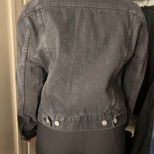 Svart jeansjacka - Snygg svart jeansjacka med knappar framtill och två bröstfickor med lock. Jackan har en klassisk krage och långa ärmar. Perfekt för en cool och avslappnad stil.