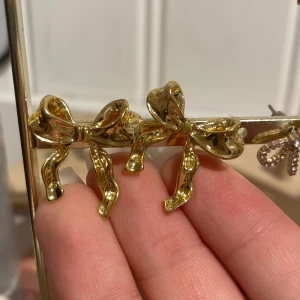 Guldiga rosettörhängen - Snygga örhängen i form av rosetter i guld. Perfekta för att ge en elegant touch till din outfit. Aldrig använda. 