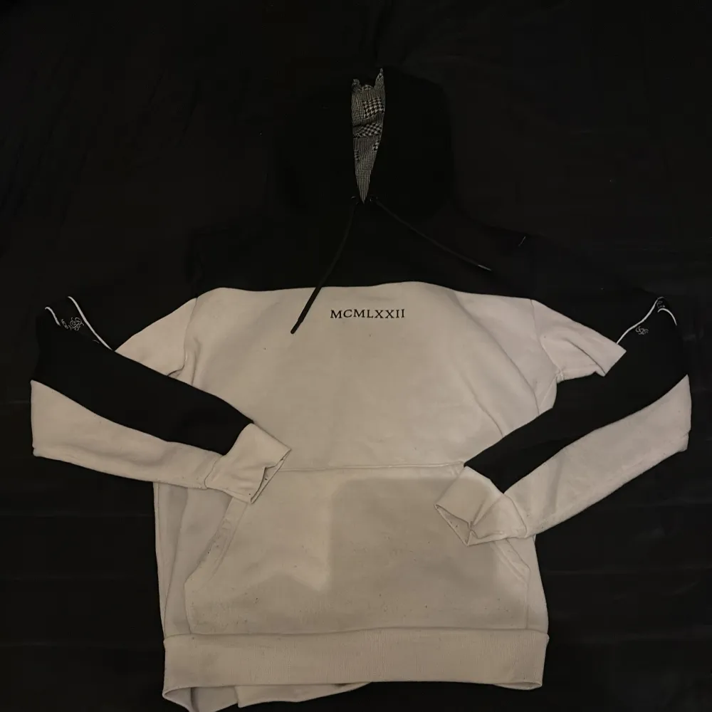 Säljer en stilren vit och svart hoodie från Brave Soul med texten 'MCMLXXII' på bröstet. Hoodien har en klassisk design med långa ärmar och en stor ficka framtill. Perfekt för en avslappnad look.. Hupparit & Collegepaidat.